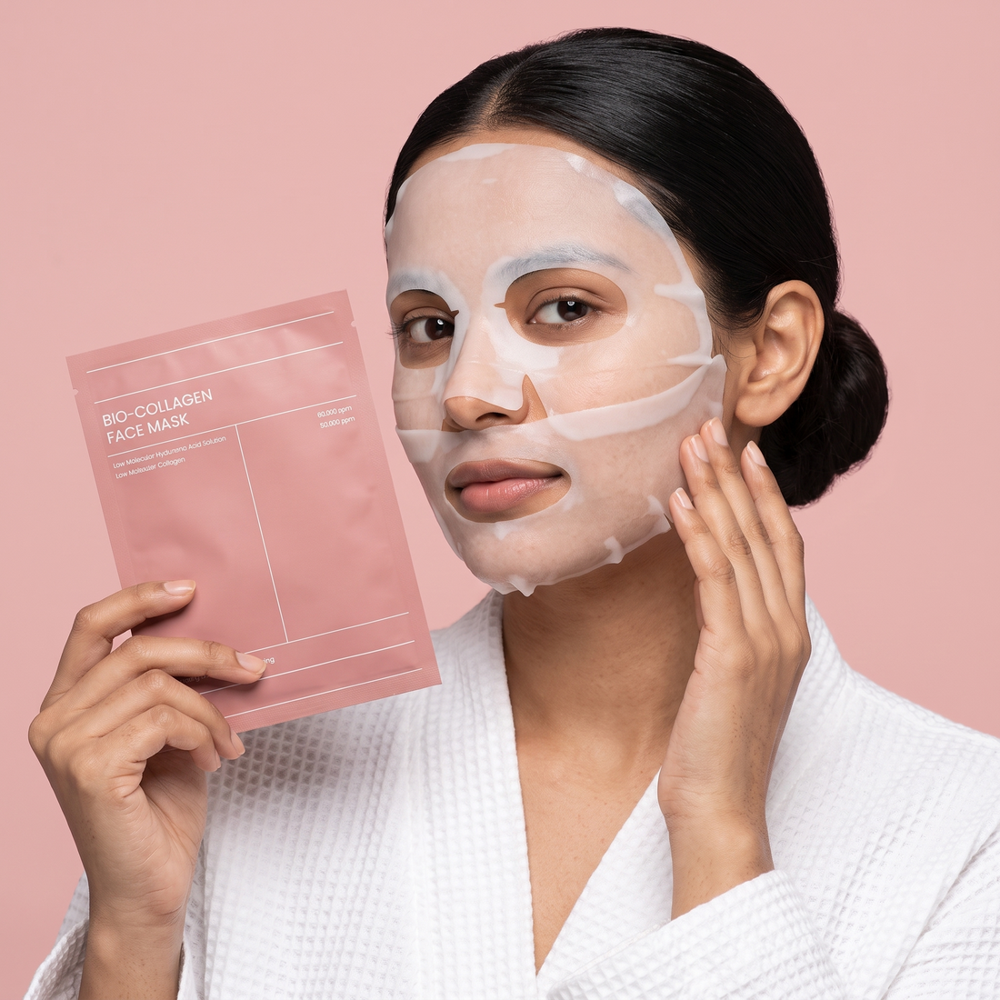 Model wearing the two-piece bio-collagen hydrogel face mask and holding the pink sachet